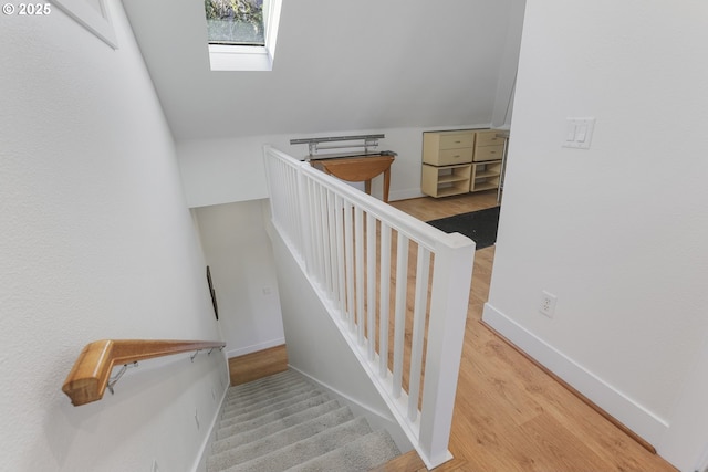 staircase featuring wood-type flooring and vaulted ceiling with skylight