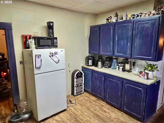 kitchen with blue cabinets, white fridge, a drop ceiling, and light wood-type flooring