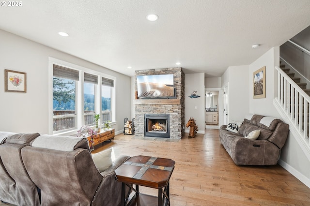 living area featuring baseboards, a textured ceiling, a fireplace, stairway, and light wood-style flooring