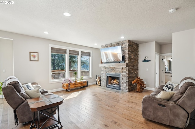 living area featuring light wood-style flooring, a textured ceiling, baseboards, and a stone fireplace
