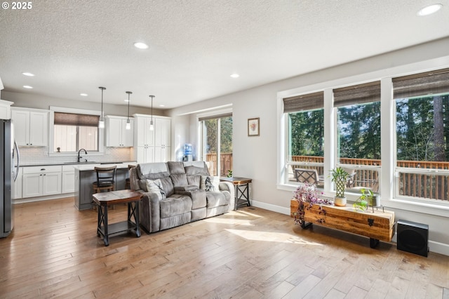 living room with light wood-style flooring, a textured ceiling, baseboards, and recessed lighting