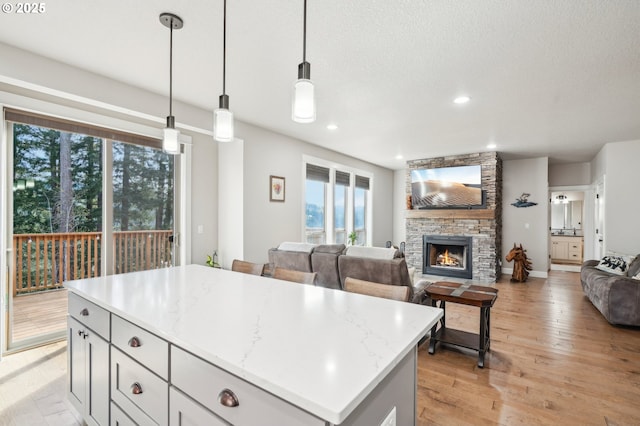 kitchen featuring a stone fireplace, open floor plan, light wood-style flooring, a center island, and pendant lighting