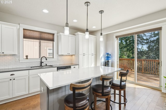 kitchen with dishwasher, a sink, a breakfast bar, light wood-style floors, and decorative backsplash