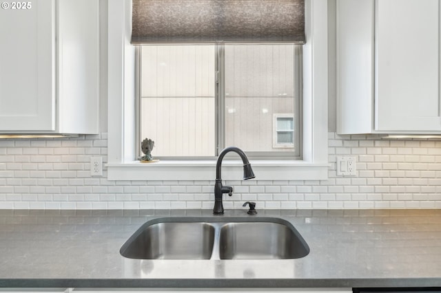 kitchen featuring white cabinets, tasteful backsplash, a sink, and dark countertops