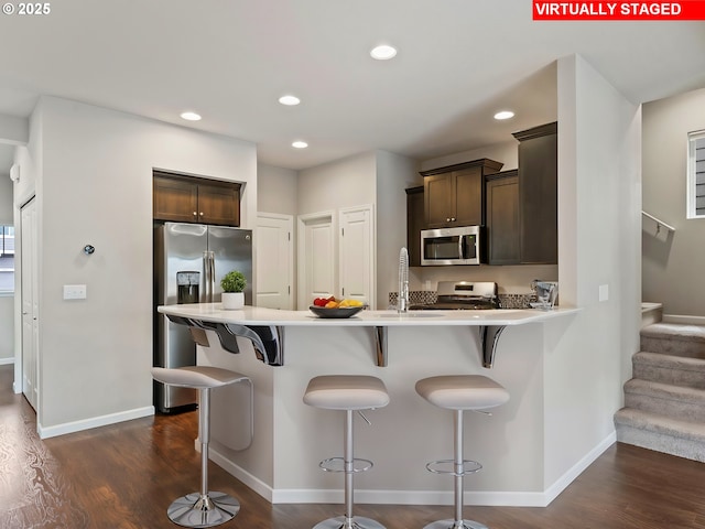 kitchen featuring dark brown cabinetry, dark wood-type flooring, stainless steel appliances, and a breakfast bar