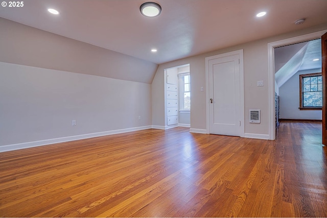 bonus room featuring lofted ceiling, light hardwood / wood-style flooring, heating unit, and a wealth of natural light