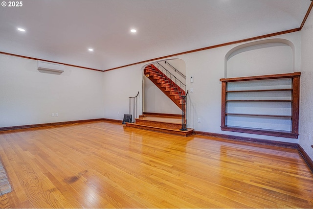 unfurnished living room featuring crown molding, a wall mounted AC, and light wood-type flooring