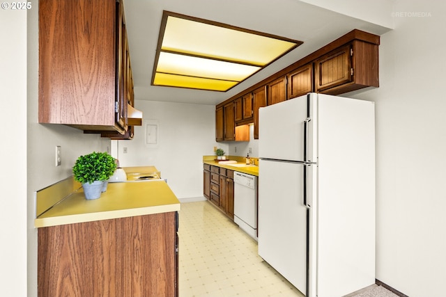 kitchen with white appliances, a sink, light flooring, under cabinet range hood, and light countertops