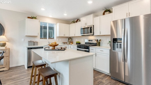 kitchen featuring appliances with stainless steel finishes, a kitchen breakfast bar, light wood-style flooring, white cabinetry, and light countertops