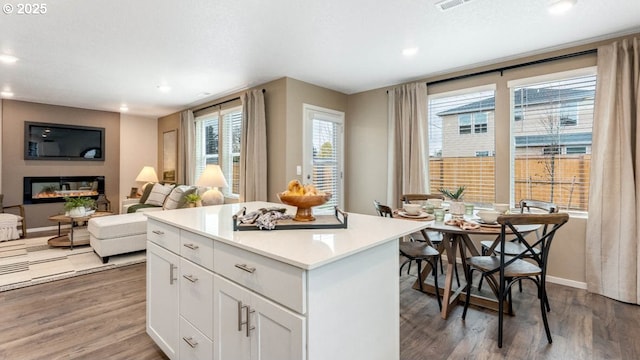kitchen featuring wood finished floors, recessed lighting, a center island, baseboards, and white cabinets