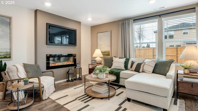 living area with light wood-style flooring, a glass covered fireplace, recessed lighting, and baseboards
