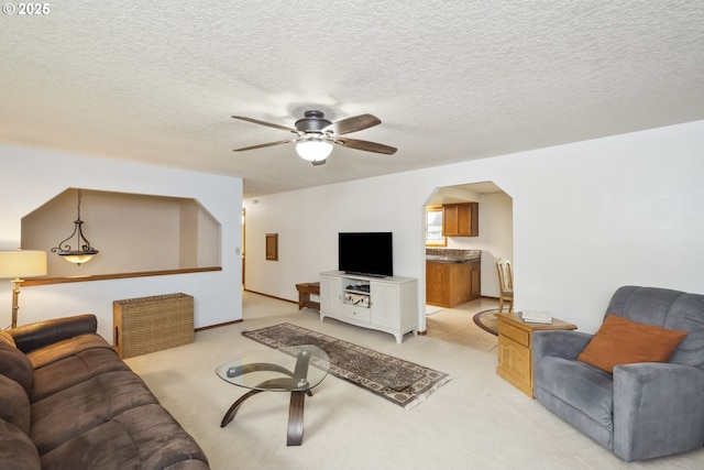 living room featuring a ceiling fan, arched walkways, light colored carpet, and a textured ceiling