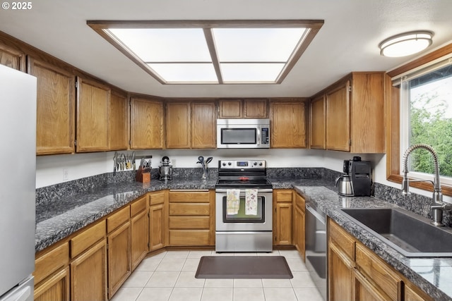 kitchen with appliances with stainless steel finishes, a sink, brown cabinetry, and light tile patterned floors