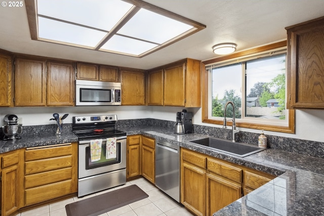kitchen with appliances with stainless steel finishes, a sink, brown cabinetry, light tile patterned floors, and tile counters