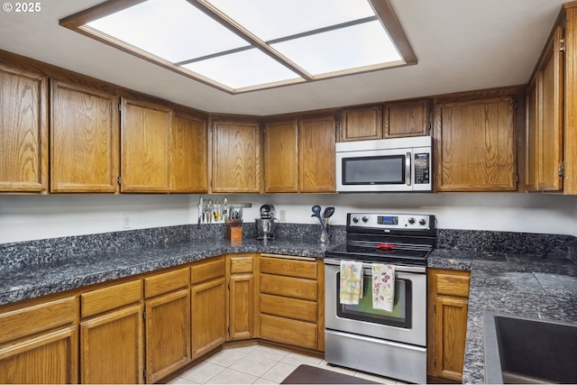 kitchen with stainless steel appliances, brown cabinets, light tile patterned floors, and dark countertops