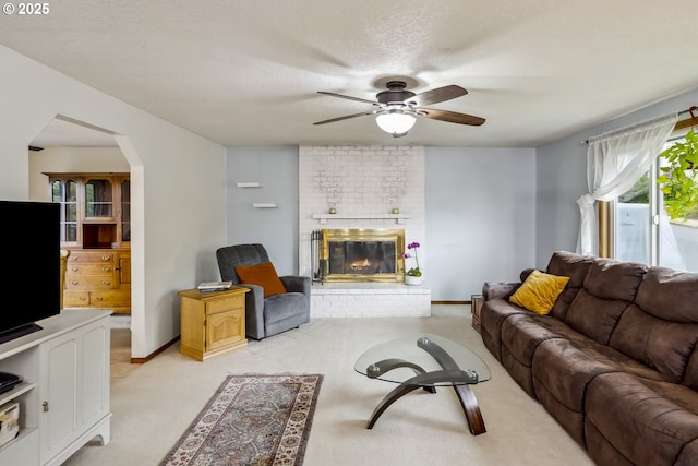 living room with a ceiling fan, arched walkways, a brick fireplace, light colored carpet, and a textured ceiling