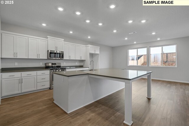 kitchen featuring stainless steel appliances, dark countertops, a sink, and wood finished floors