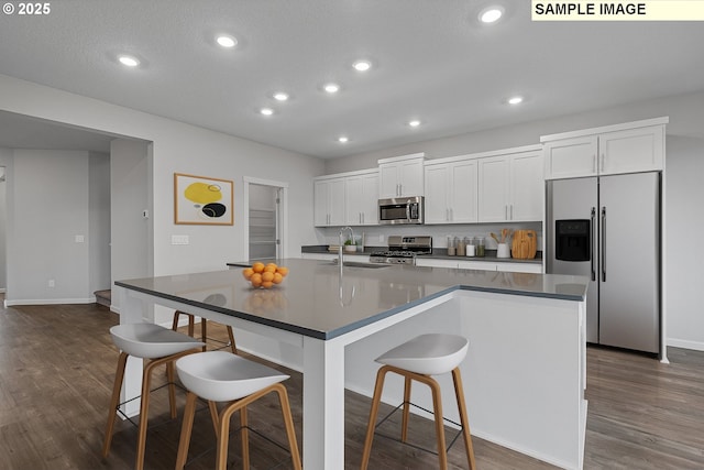 kitchen featuring a breakfast bar, white cabinets, a center island with sink, sink, and stainless steel appliances