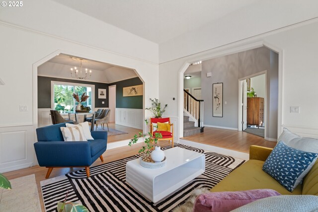 living area featuring a chandelier, wood finished floors, stairs, wainscoting, and arched walkways