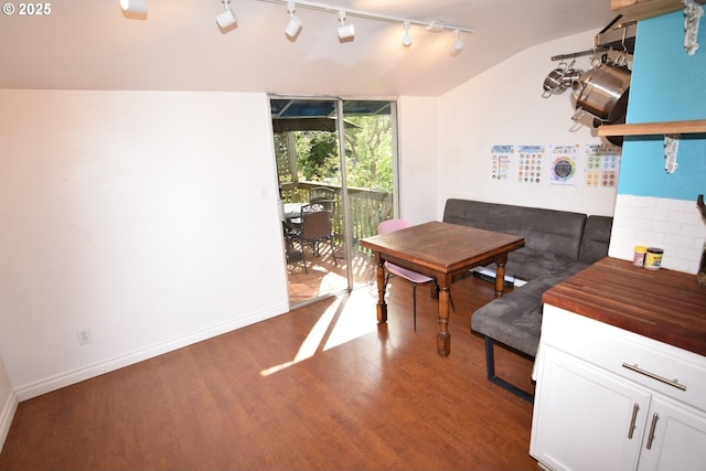 dining area with baseboards, track lighting, wood finished floors, and lofted ceiling