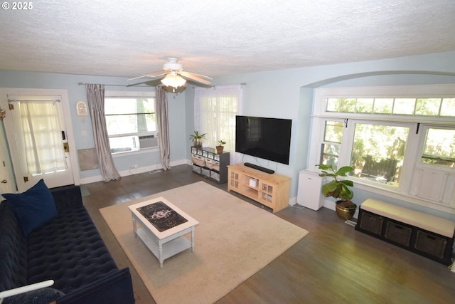 living area with baseboards, ceiling fan, dark wood finished floors, and a textured ceiling
