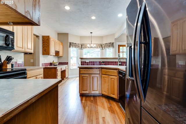 kitchen with sink, black appliances, decorative light fixtures, a chandelier, and light wood-type flooring