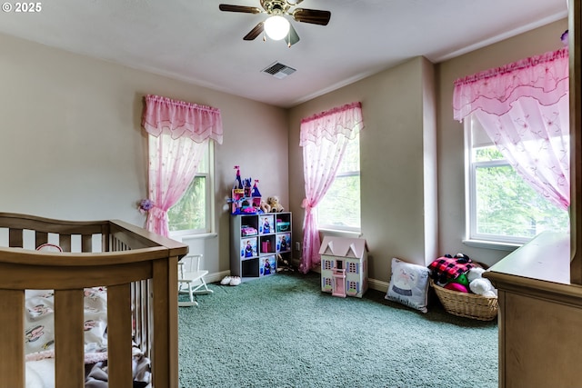 bedroom featuring multiple windows, a crib, ceiling fan, and carpet