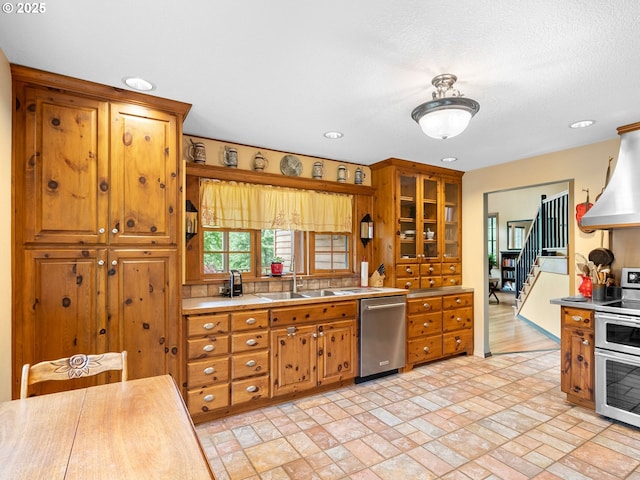 33901 Merrill Creek Rd, Deer Island, OR 97054 - kitchen with stainless steel appliances, brown cabinetry, wall chimney exhaust hood, a sink, and glass insert cabinets
