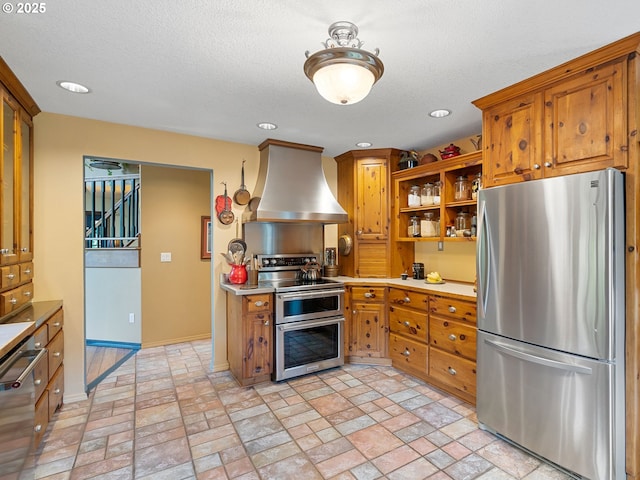 33901 Merrill Creek Rd, Deer Island, OR 97054 - kitchen with stainless steel appliances, wall chimney range hood, brown cabinetry, brick patterned flooring, and recessed lighting