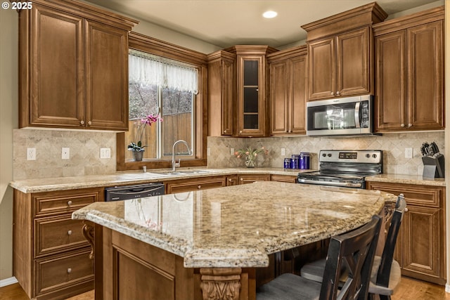 kitchen with light stone counters, a breakfast bar, a sink, appliances with stainless steel finishes, and decorative backsplash