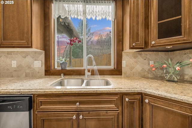 kitchen with stainless steel dishwasher, a sink, glass insert cabinets, and brown cabinets