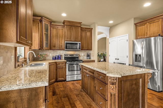 kitchen with light stone counters, dark wood finished floors, tasteful backsplash, appliances with stainless steel finishes, and a sink