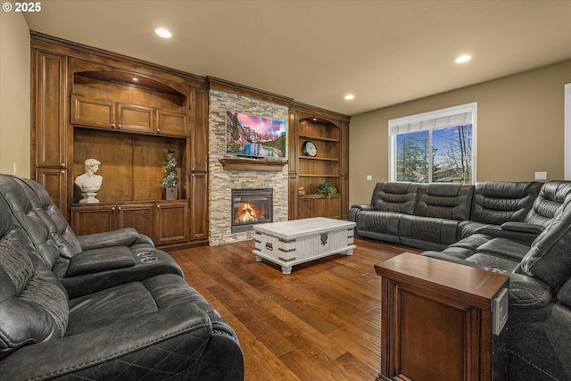 living room featuring recessed lighting, dark wood-style flooring, and a stone fireplace