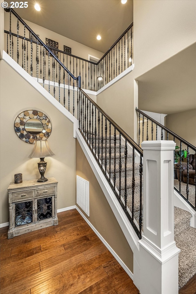 stairs featuring baseboards, visible vents, a towering ceiling, and hardwood / wood-style floors