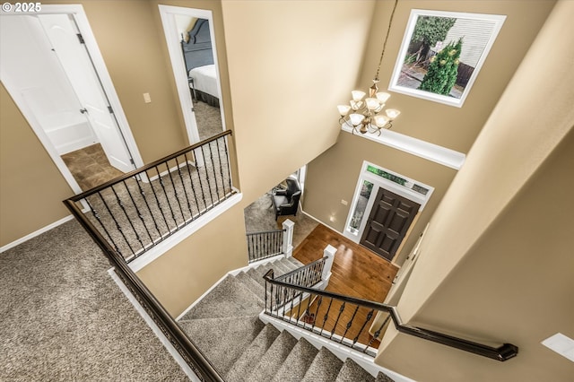 foyer entrance with a towering ceiling, stairway, an inviting chandelier, carpet flooring, and baseboards