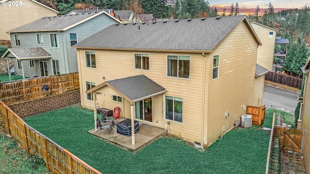 back of property at dusk featuring a patio area, a fenced backyard, a yard, and roof with shingles