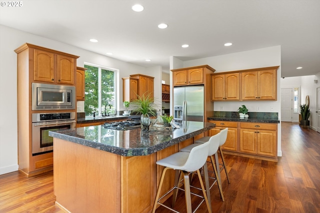 12988 NW Tigon Ln, Portland, OR 97229 - kitchen featuring appliances with stainless steel finishes, a center island, recessed lighting, dark wood-type flooring, and brown cabinetry