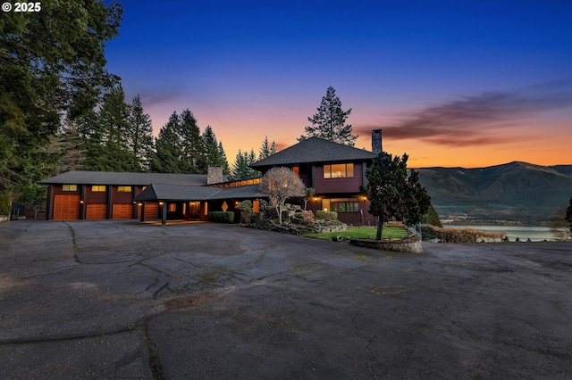 view of front of home featuring aphalt driveway, a chimney, an attached garage, and a water and mountain view