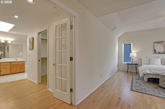 bedroom featuring sink, a textured ceiling, lofted ceiling, connected bathroom, and light hardwood / wood-style flooring