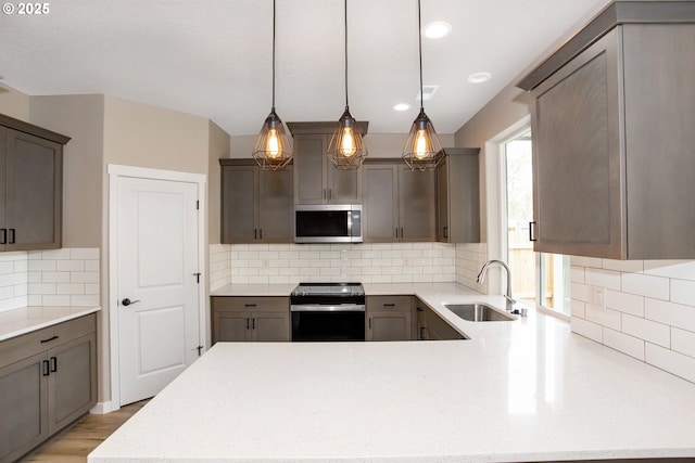 kitchen with a sink, stainless steel microwave, tasteful backsplash, hanging light fixtures, and black electric range oven