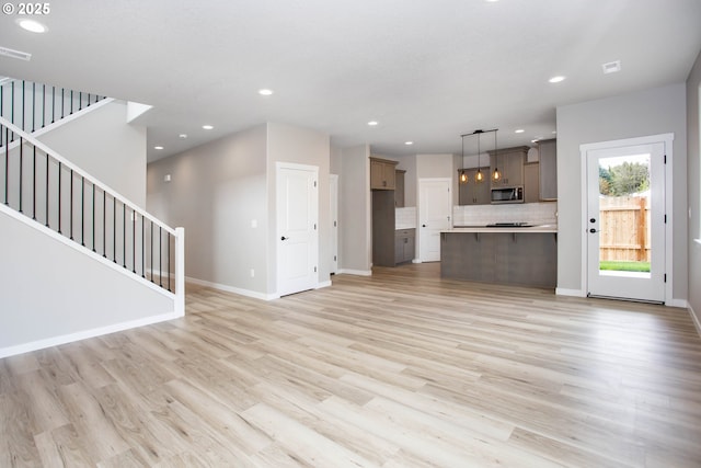 unfurnished living room with stairway, baseboards, recessed lighting, and light wood-style flooring
