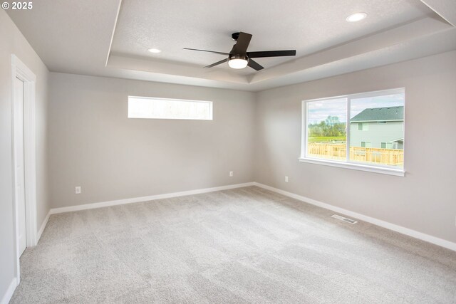 spare room with ceiling fan, carpet floors, a tray ceiling, baseboards, and visible vents