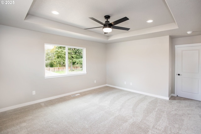 spare room featuring a ceiling fan, light carpet, a raised ceiling, baseboards, and visible vents
