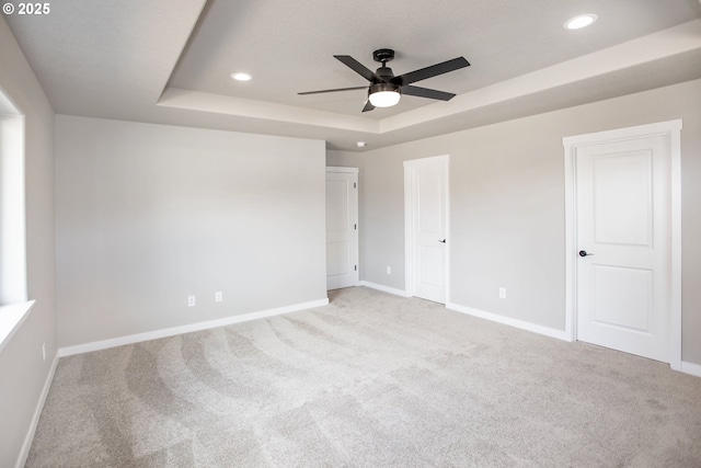 unfurnished bedroom with recessed lighting, light carpet, a tray ceiling, and baseboards