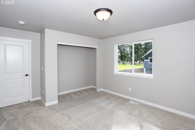 unfurnished bedroom featuring a textured ceiling, a closet, carpet floors, baseboards, and visible vents