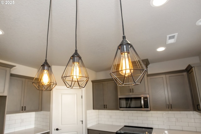 kitchen featuring stainless steel microwave, visible vents, backsplash, stove, and light countertops