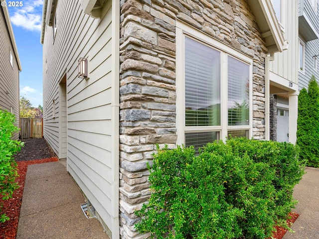 view of side of property with stone siding and fence