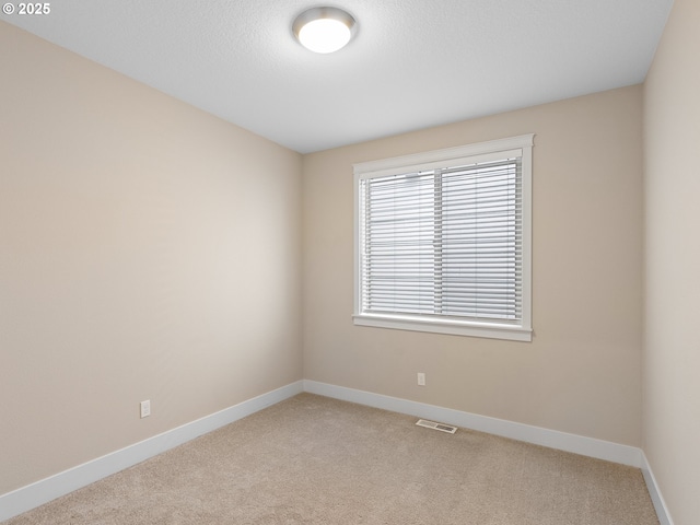 empty room featuring baseboards, visible vents, and light carpet