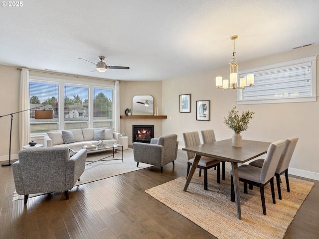 dining space with dark wood finished floors, visible vents, ceiling fan with notable chandelier, and a tiled fireplace