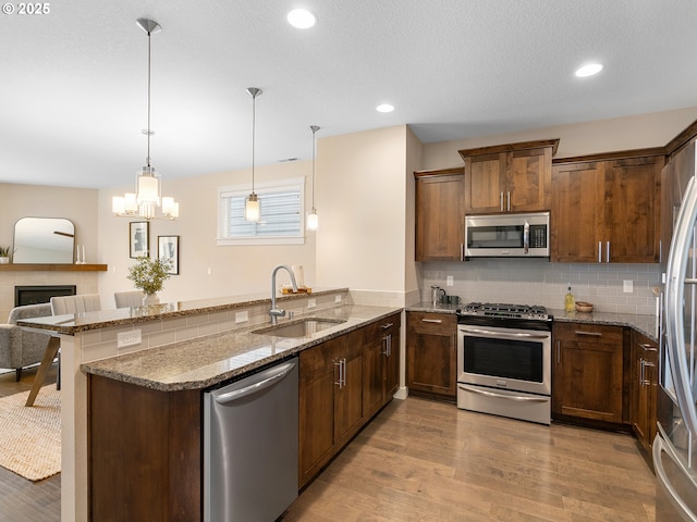 kitchen with light wood finished floors, a peninsula, a sink, appliances with stainless steel finishes, and tasteful backsplash